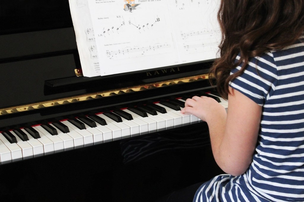 A young child playing piano out of a music book
